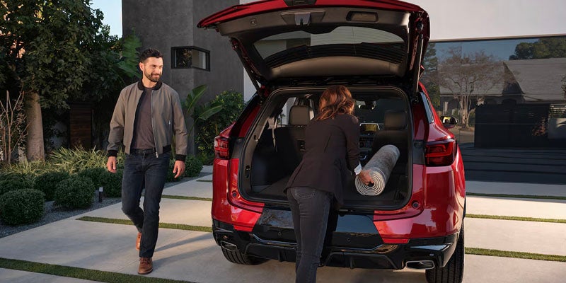 Chevrolet Blazer car with Woman loading a rolled-up rug into the trunk while and man near there