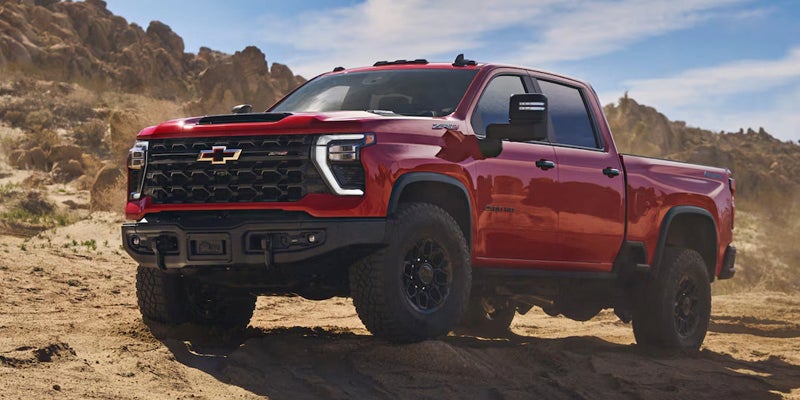 2025 Chevrolet Silverado 2500 HD red on the sand rocky hills in the background